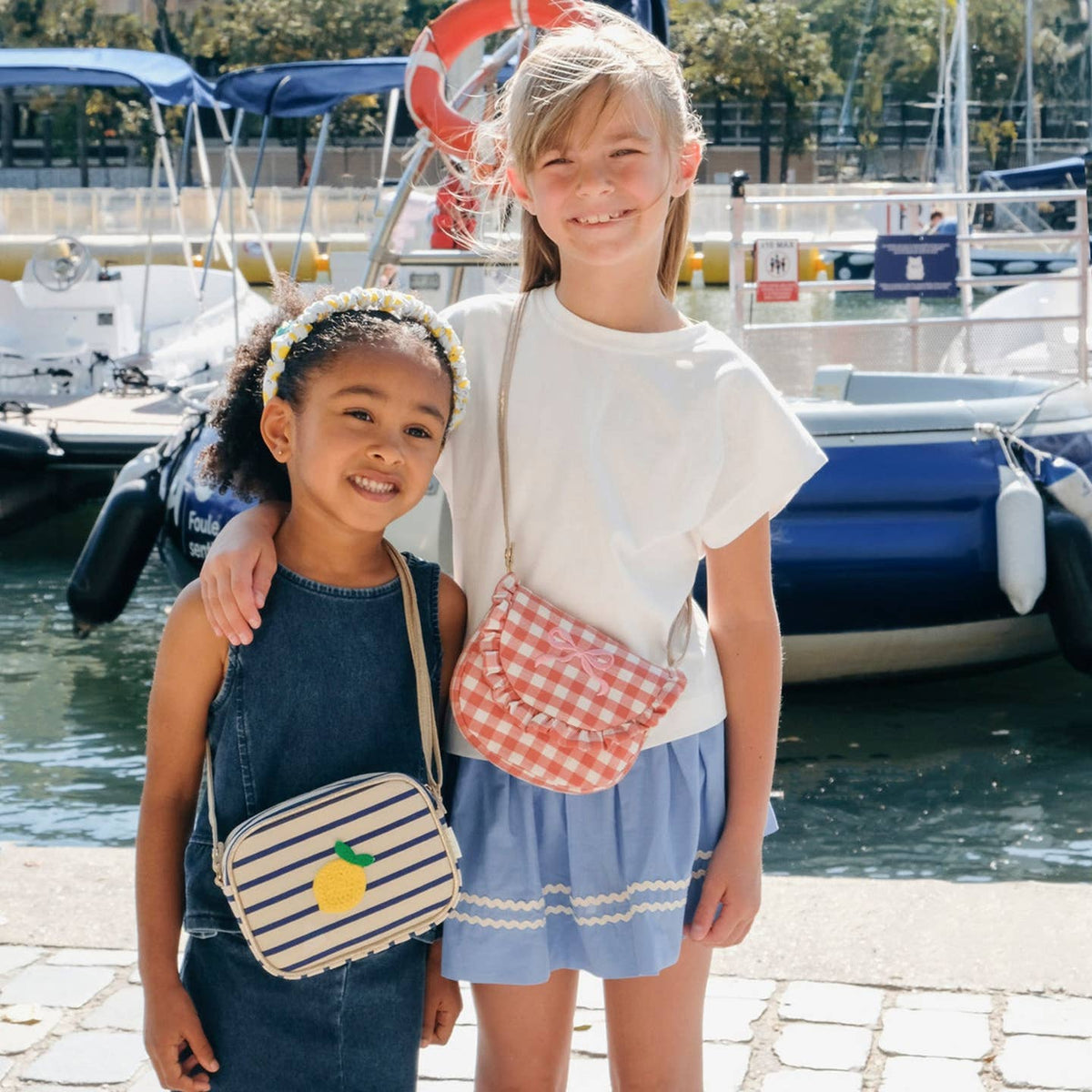 Two young girls standing by a marina with boats in the background