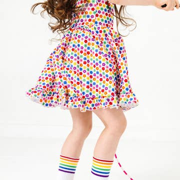 Child wearing a colorful polka dot dress and rainbow striped socks on a white background