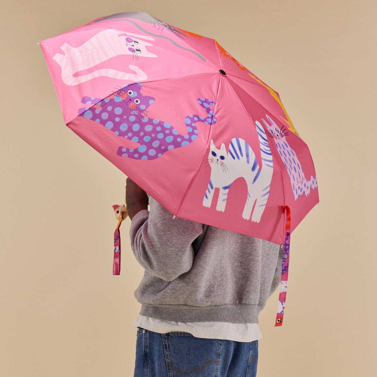 Person holding a pink umbrella with animal illustrations on a beige background
