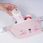 Pink pouch with cat face design and teddy bear inside, held by a hand on a light gray background