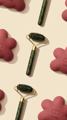 Two green skin care rollers with gold accents on a beige background with pink silicone masks.