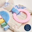Baby toy with textured elements and a pink ring on a soft fabric background
