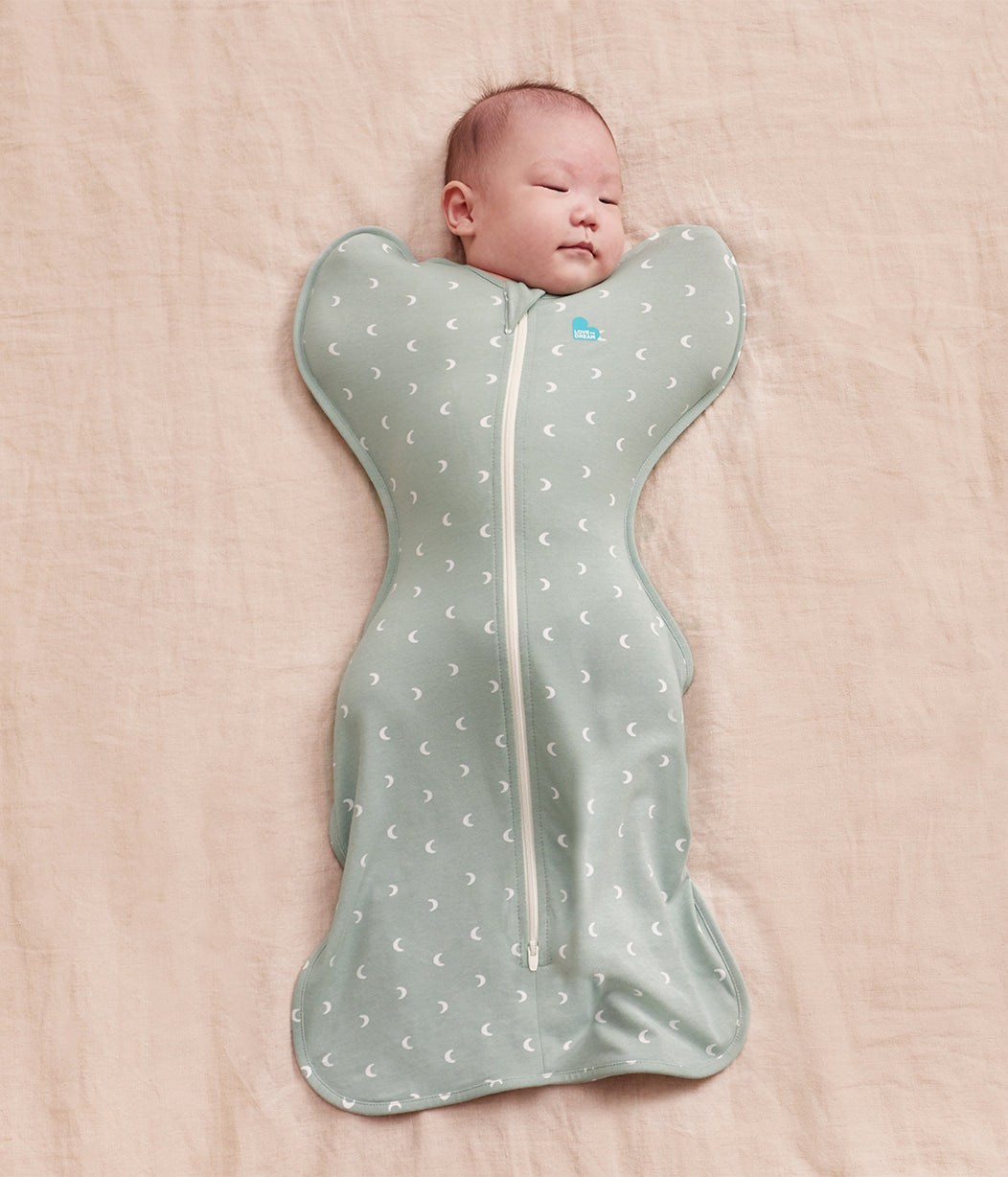 Baby wrapped in a gray swaddle with moon patterns on a pink blanket