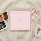Pink baby album with ultrasound photo, footprint, and ribbon on a soft fabric background
