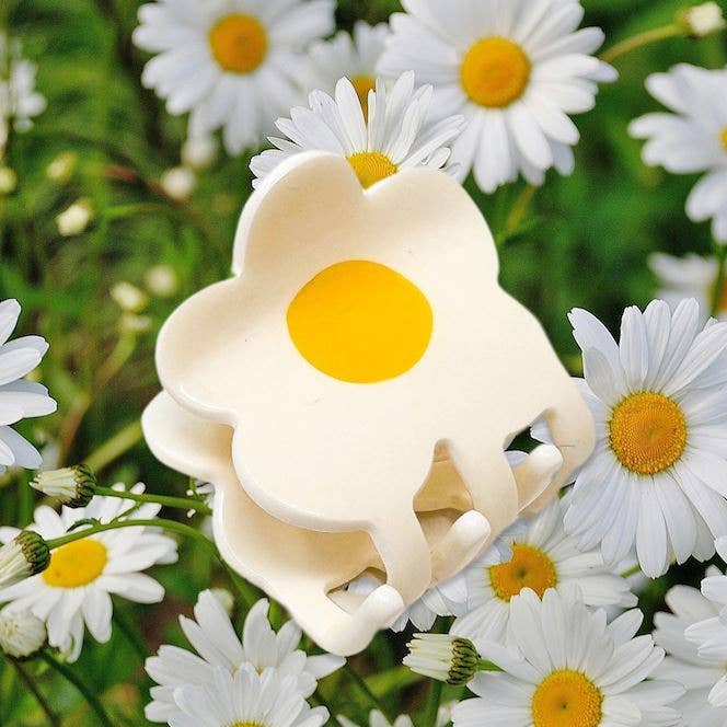 Flower-shaped object with yellow center surrounded by white flowers with yellow centers on a green background