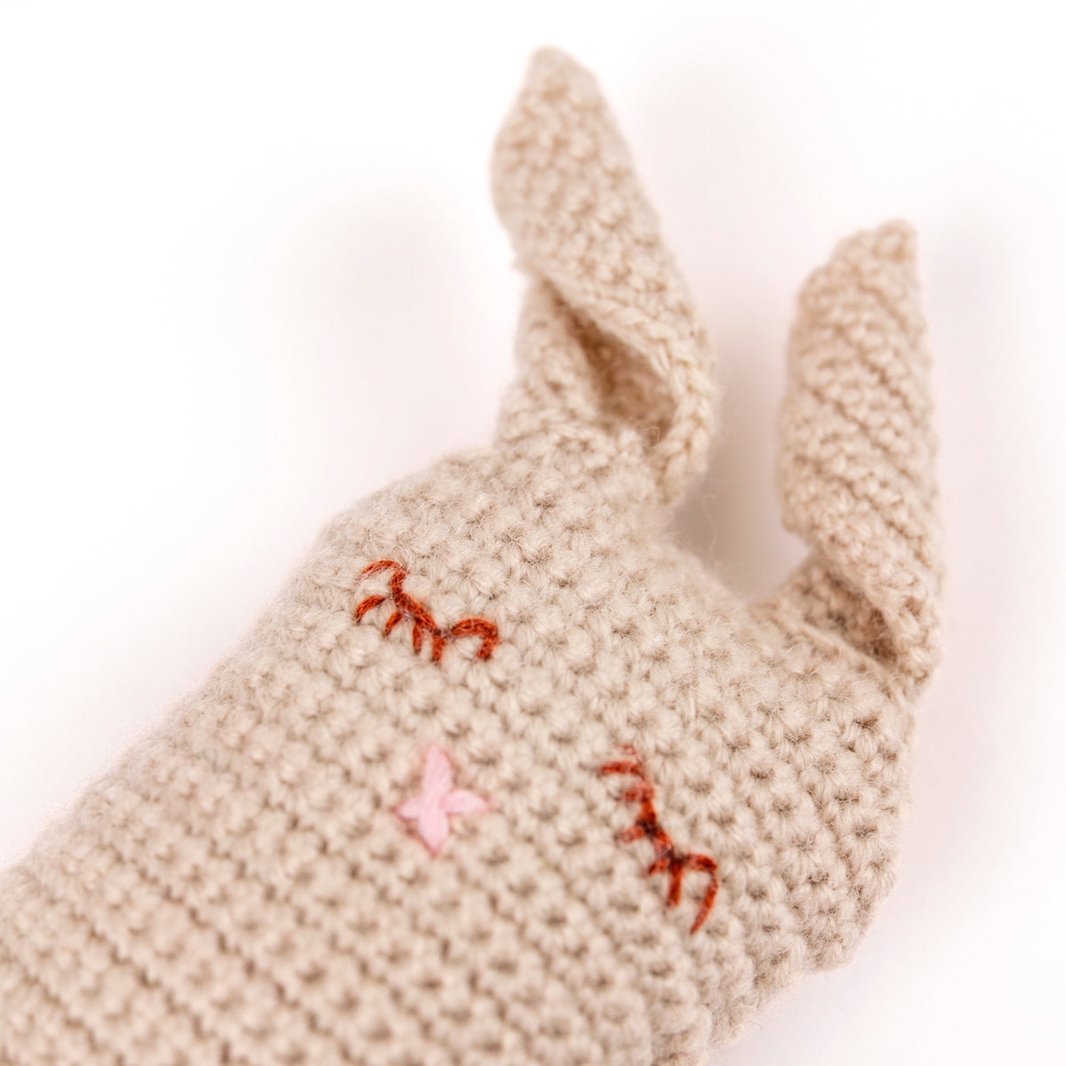 Beige knitted bunny with embroidered details on a white background