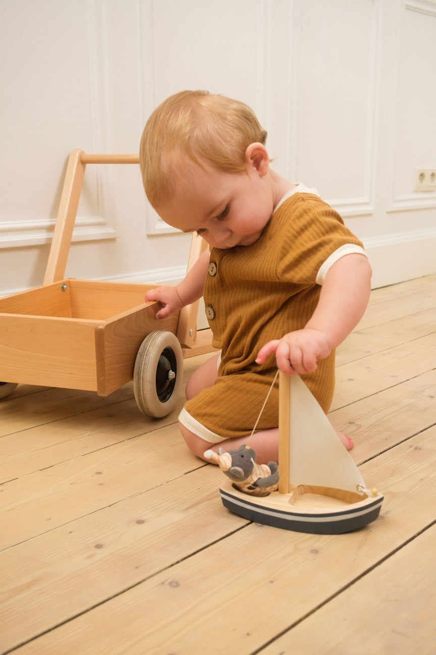 Child playing with a toy sailboat on a wooden floor