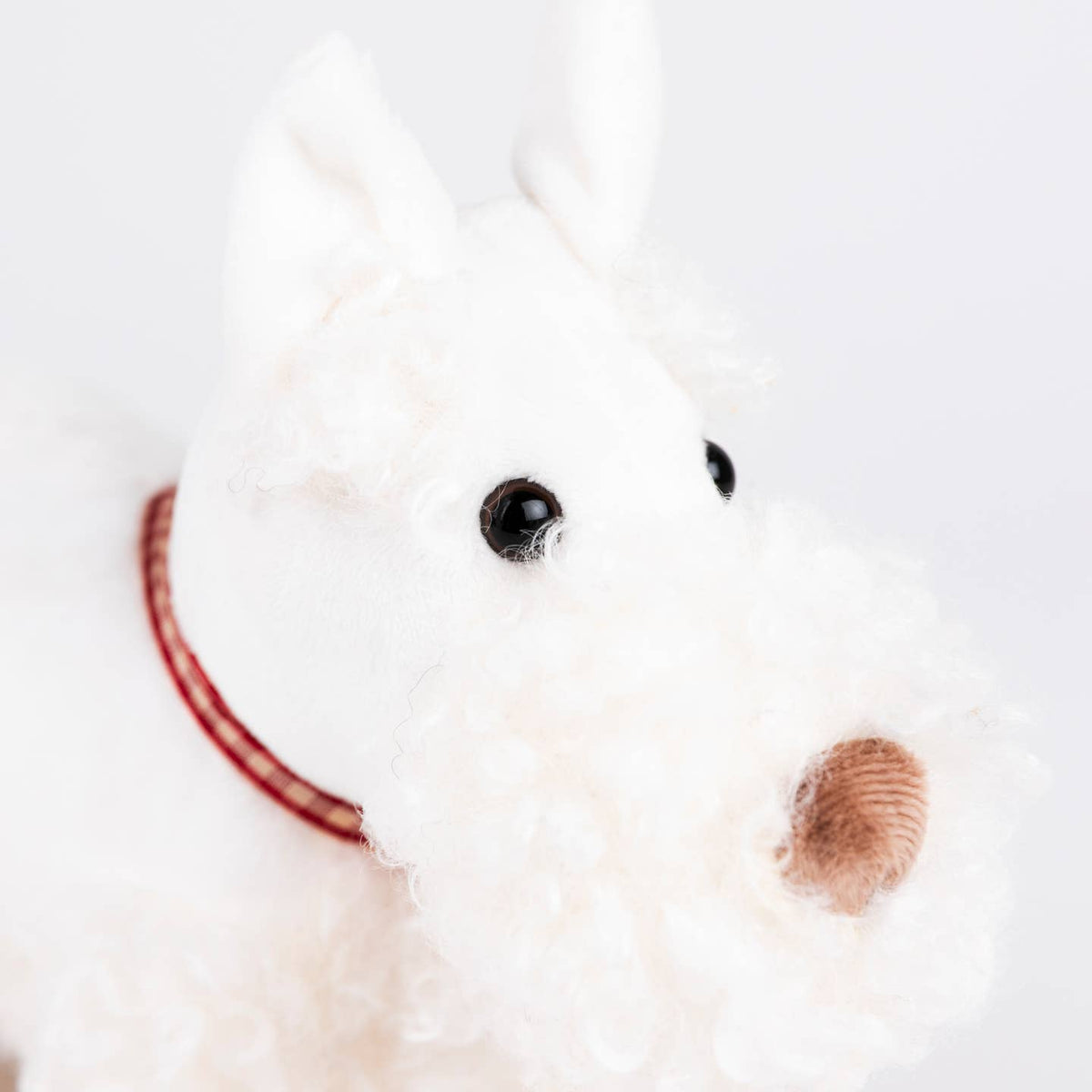 Close-up of a white plush toy with a red ribbon on a light background