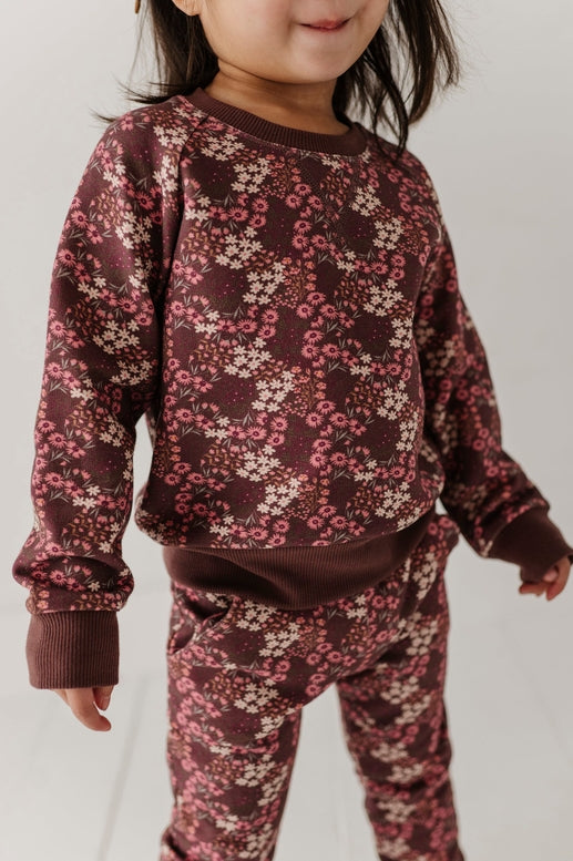 Child wearing a maroon floral outfit on a plain background