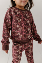 Child wearing a maroon floral outfit on a plain background