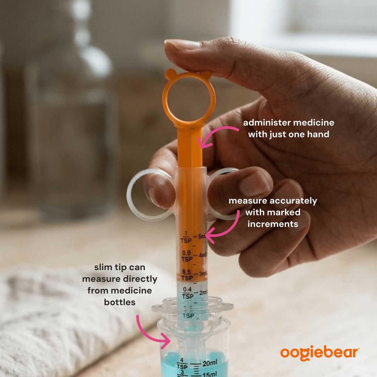 A hand holds a transparent syringe-style measuring device with an orange top loop and pink measurement markings, shown with overlaid text explaining how to administer medicine and measure accurately. The background is a softly blurred indoor setting.