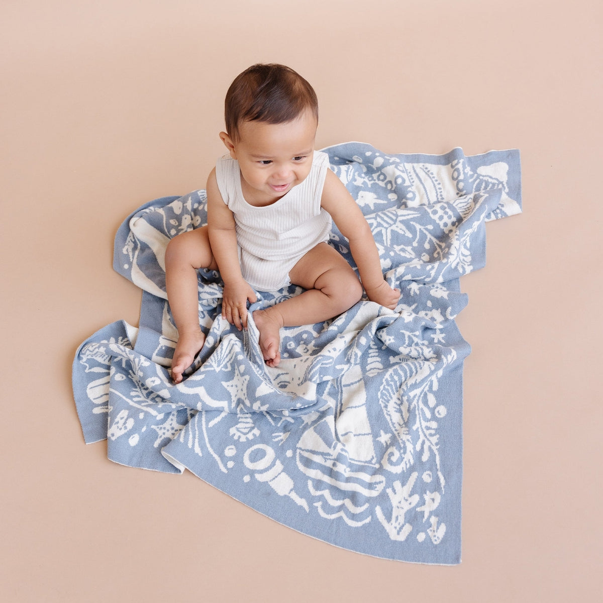 Baby sitting on a blue patterned blanket against a beige background