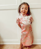 Child wearing a floral dress standing against a white paneled wall.