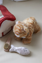 Plush tiger toy with a fish-shaped toy and a brush on a light surface
