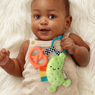 Baby holding a colorful teething toy with a green fish attachment on a white fluffy surface