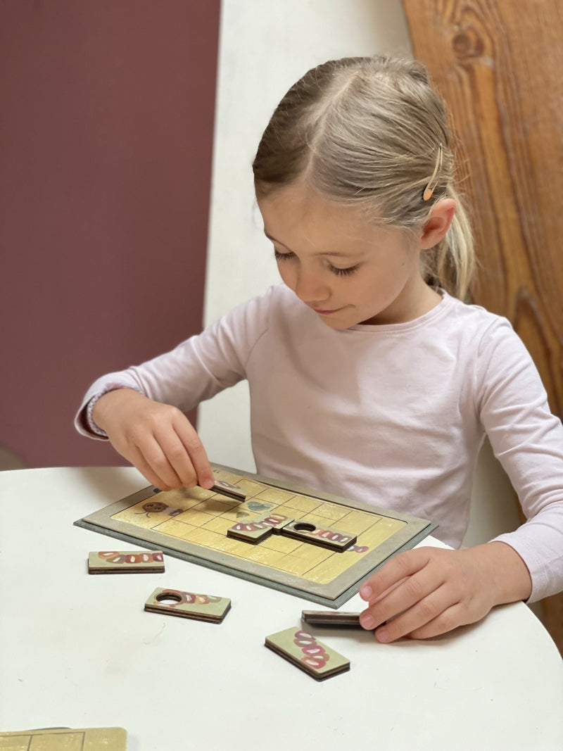 Young girl playing a board game at a table with a wooden chair in the background.