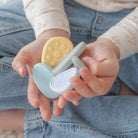 Baby hands holding two silicone teething rings, one yellow and one light blue, against a denim background.