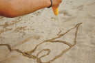 Person drawing a design in sand with a yellow tool