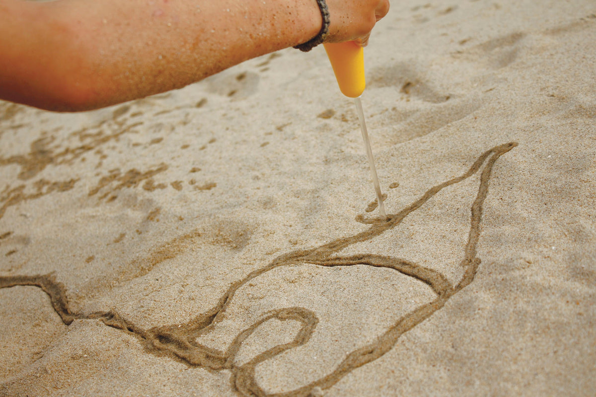 Person drawing a design in sand with a yellow tool