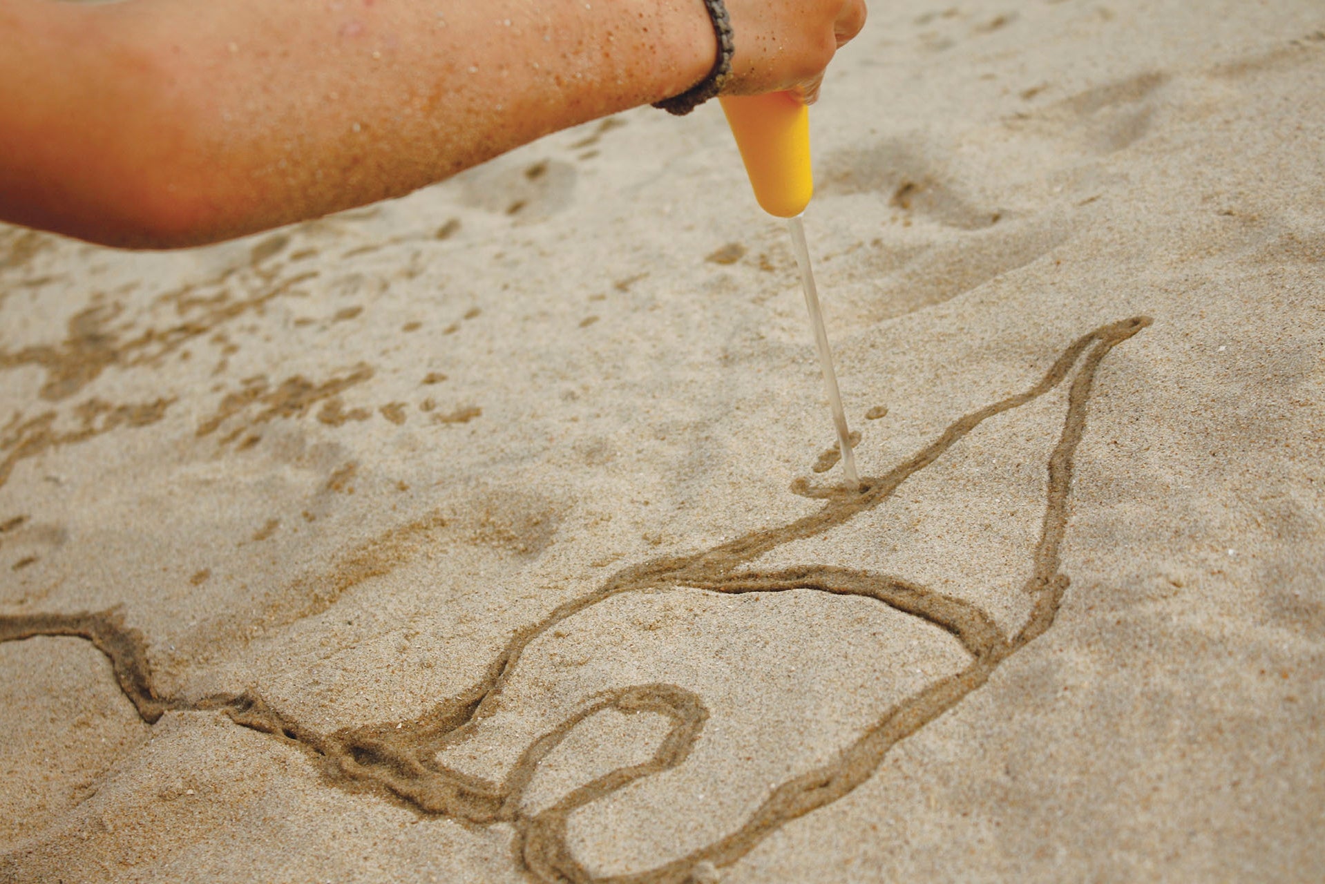 Person drawing a design in sand with a yellow tool