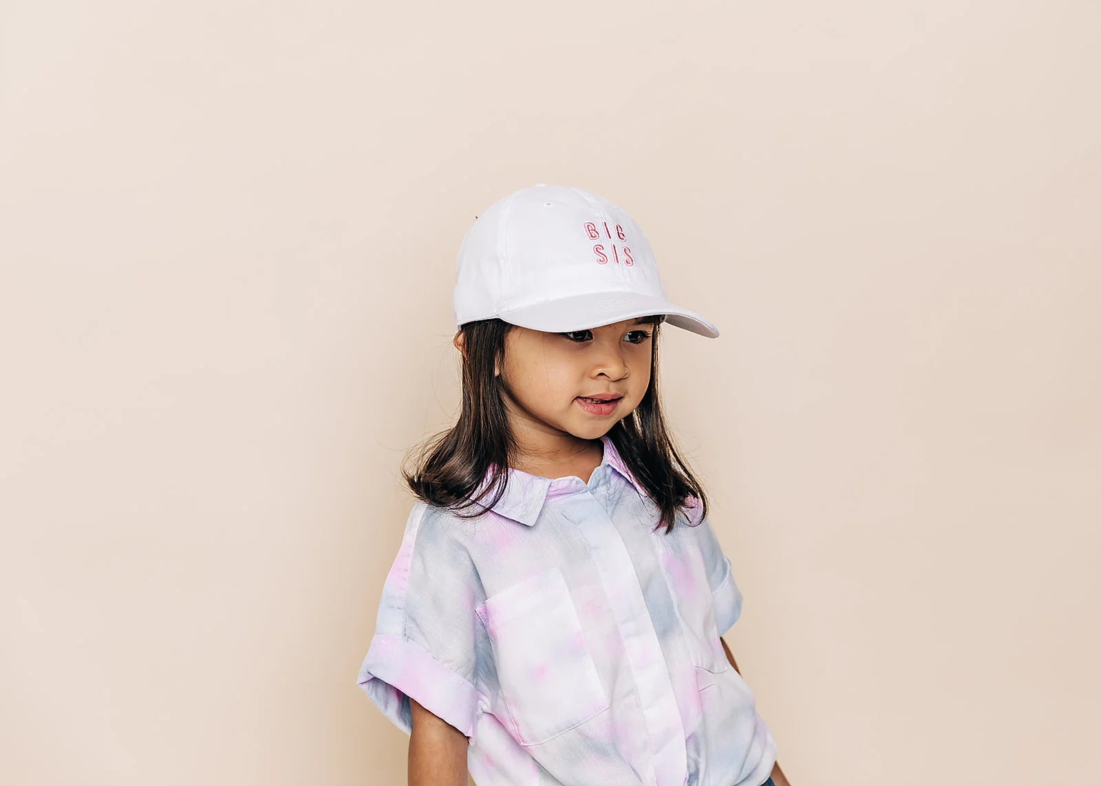 Child wearing a white cap with 'BIG SIS' text on a beige background