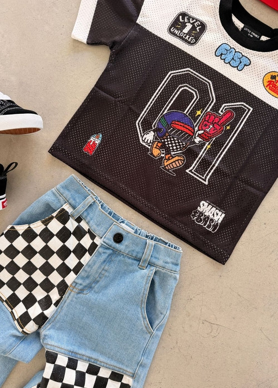 Black t-shirt with colorful graphics, blue jeans, and checkered shoes on a beige surface