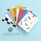 Stack of colorful greeting cards with geometric designs on a light blue background