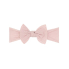 A light pink fabric headband with a large bow in the center, photographed flat against a solid white background.