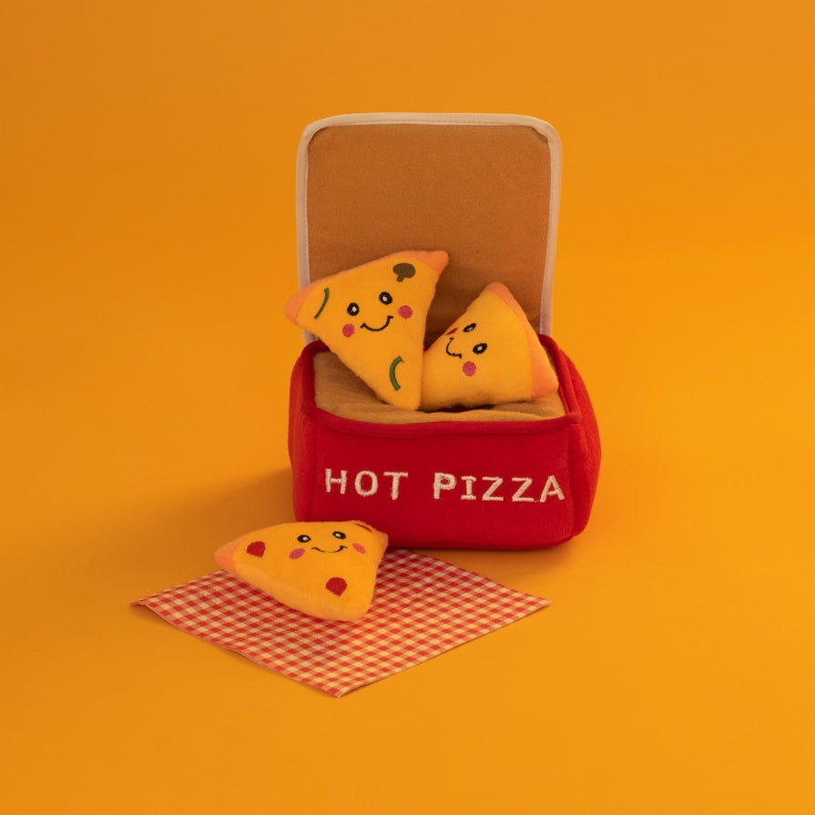 A cute plush toy set featuring two smiling pizza slice characters sitting inside a red fabric hot pizza container labeled 'HOT PIZZA', with one slice resting on a red-and-white checkered napkin in front, all set against a solid orange background.