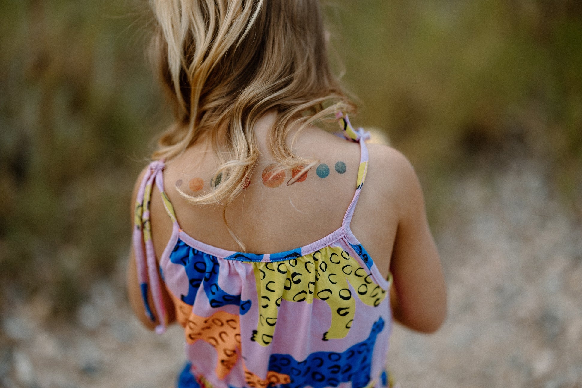 Child wearing a colorful dress with animal prints, standing outdoors with a blurred natural background.