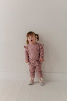 Child wearing a pink outfit with ruffled sleeves against a white background