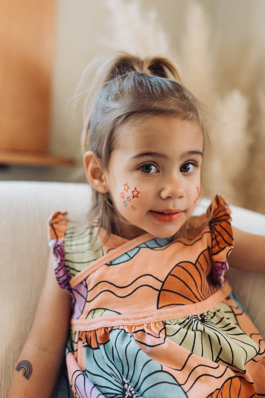 Young girl wearing a colorful dress with floral patterns, sitting on a couch.