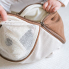 Close-up of a mesh pouch with a brown zipper held by hands on a light background
