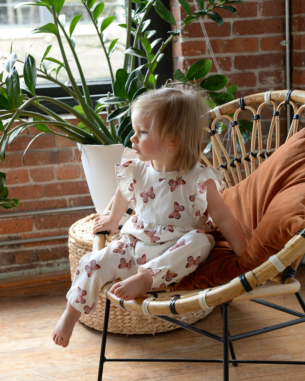 Child sitting on a wicker chair with plants in the background