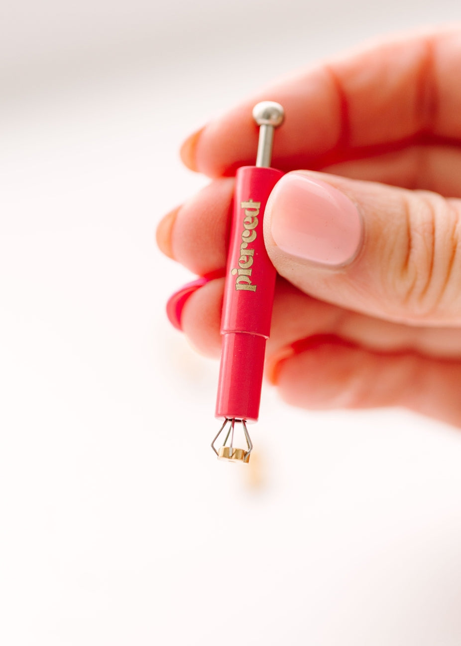 A hand holding a red and silver jewelry piercing tool with the brand name 'piercet' printed vertically on the handle, set against a clean white background.