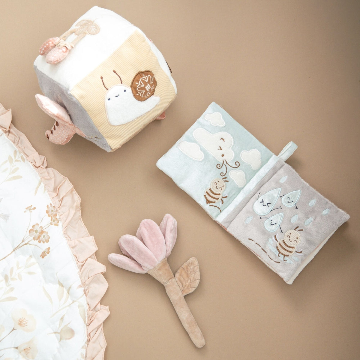 Baby items including a plush toy, blanket, and rattle on a beige background