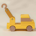 Wooden toy crane with yellow body and brown hook on a beige background