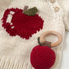 Crocheted red apple teether attached to a knitted fabric with an embroidered apple design.