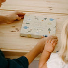 Person and child holding hands over a children's book on a wooden surface