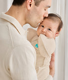 Man holding a baby in a beige baby carrier against a white background