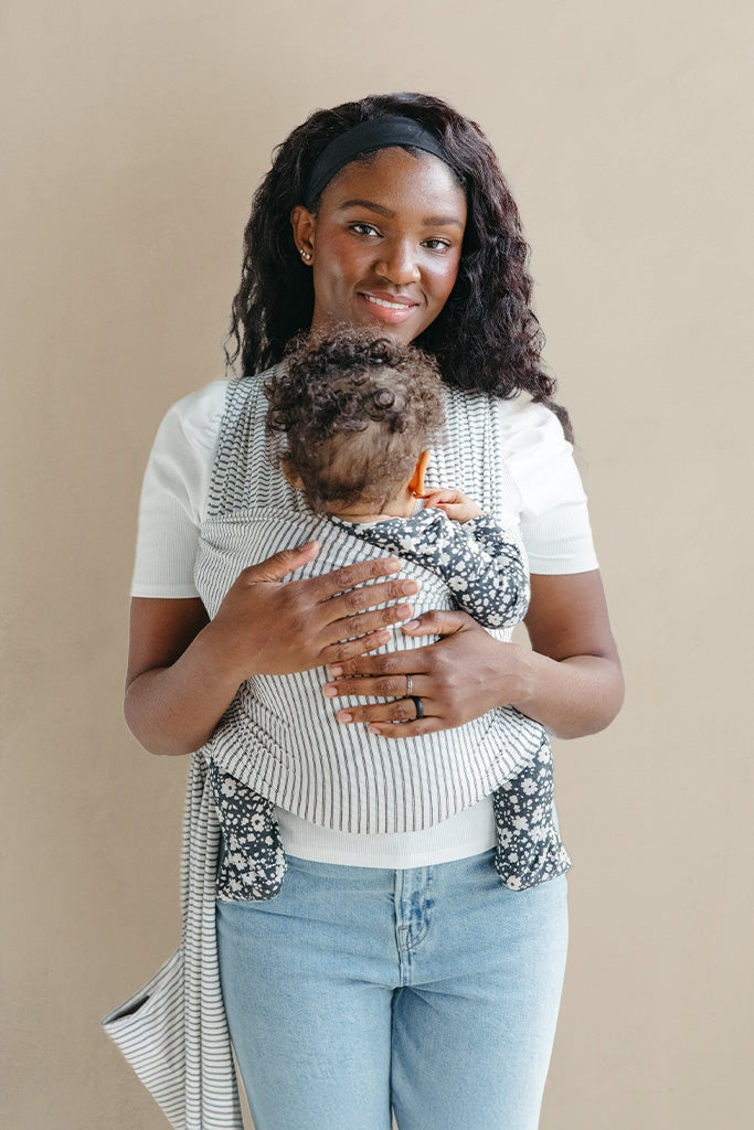 Woman holding a baby in a sling against a beige background
