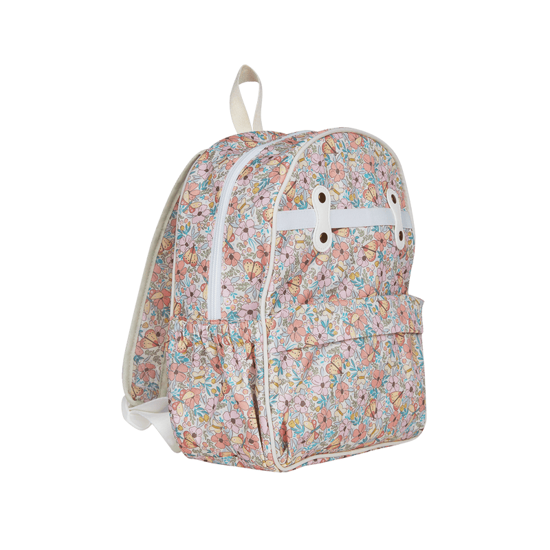 A small backpack with a pastel floral and butterfly pattern on a light pink background, featuring a white horizontal strap across the top front with two gold-tone grommets and a cream-colored top handle, shown against a plain white background.