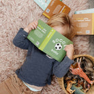Child playing with 'Soccer Baby' toy packaging on a pink carpet