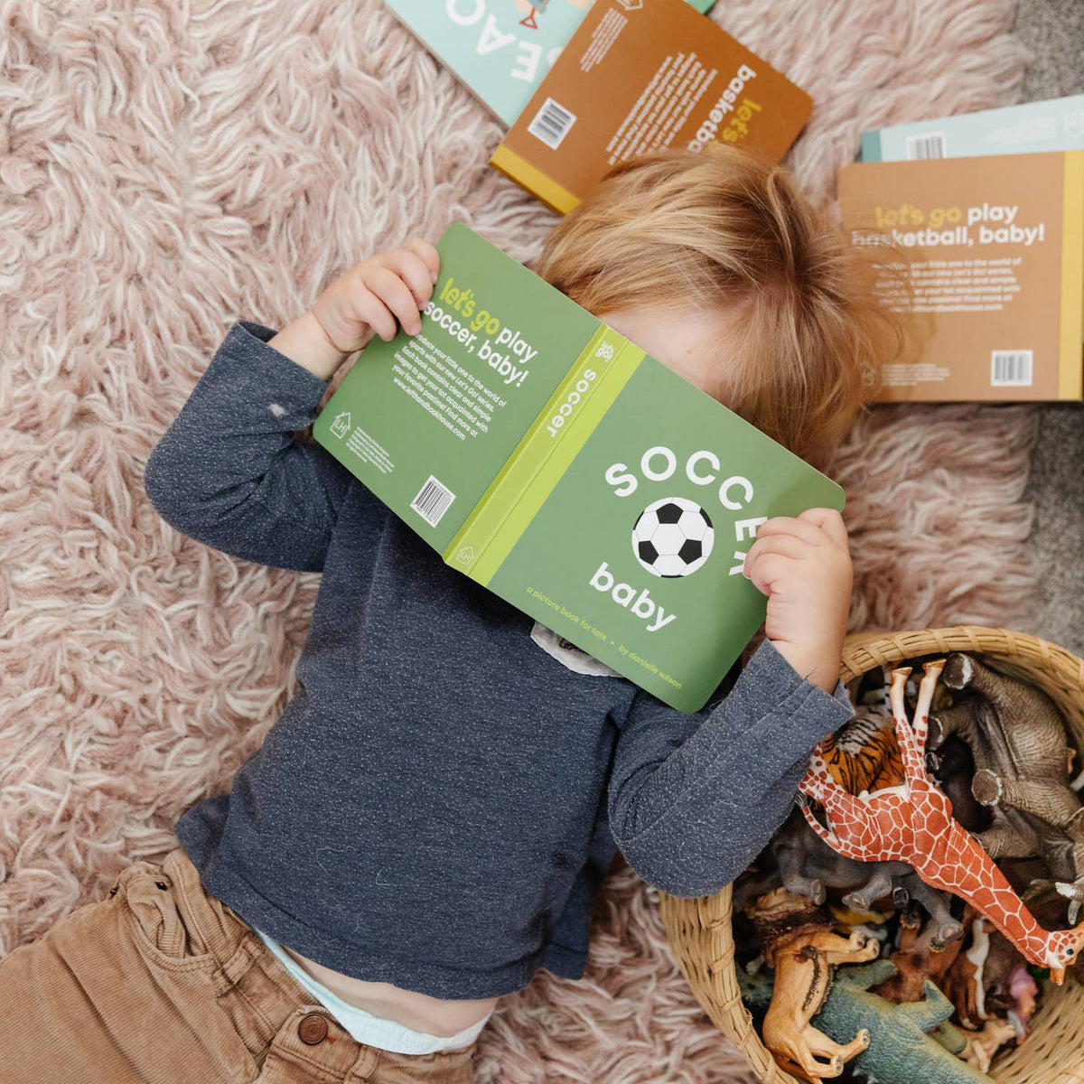 Child playing with 'Soccer Baby' toy packaging on a pink carpet