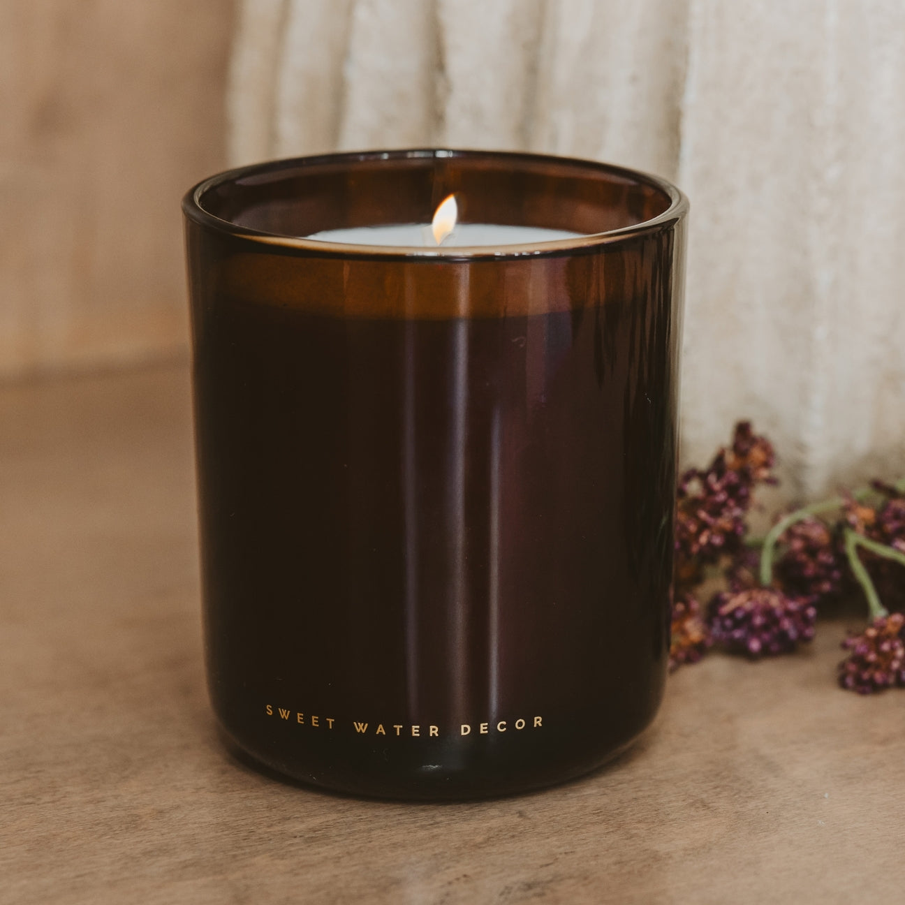 Brown candle with 'Sweet Water Decor' branding on a neutral background