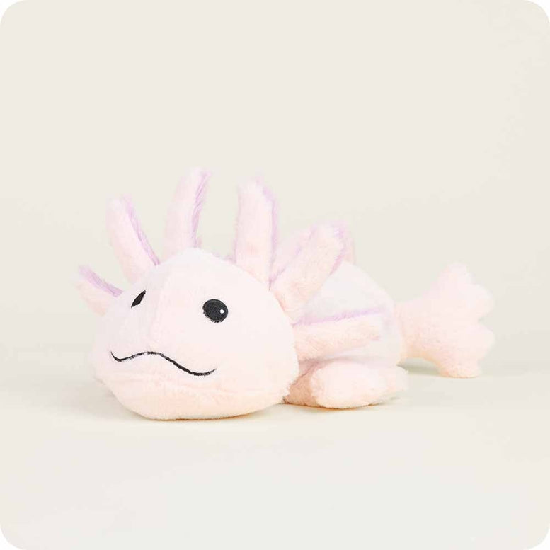 A side-angle view of the Pink Axolotl by Warmies plush toy resting on a neutral surface, showcasing its soft light pink body, embroidered smiling face, and fluffy external gills.