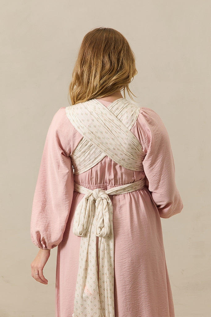 A woman shown from the back wearing a dusty pink long-sleeve dress with a cream patterned wrap belt tied around her waist, set against a plain beige studio background.