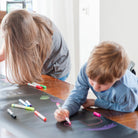 Woman and child drawing on a large piece of paper with markers.
