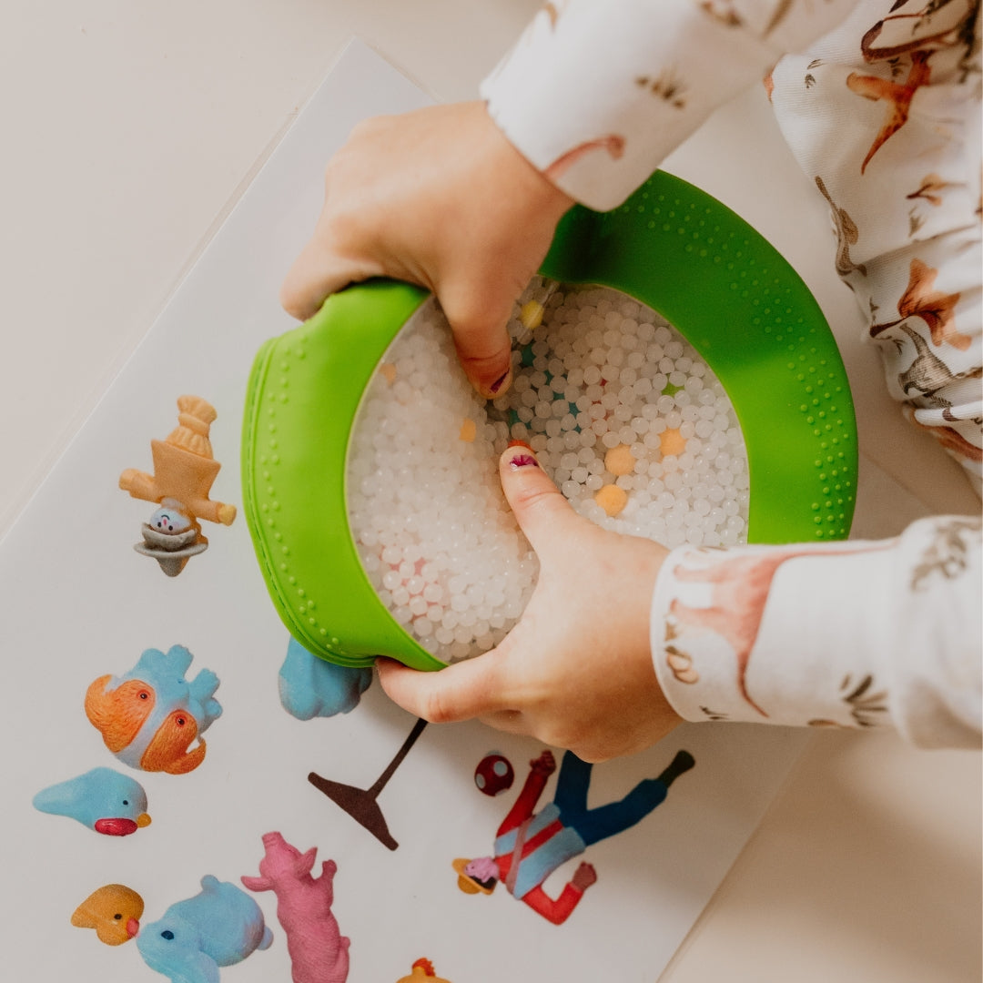 Child playing with a green toy and colorful figurines on a light surface
