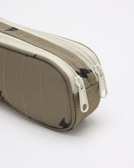 A close-up of a taupe-colored zippered pouch or pencil case with a textured surface and white zipper pulls, shown on a light gray background.